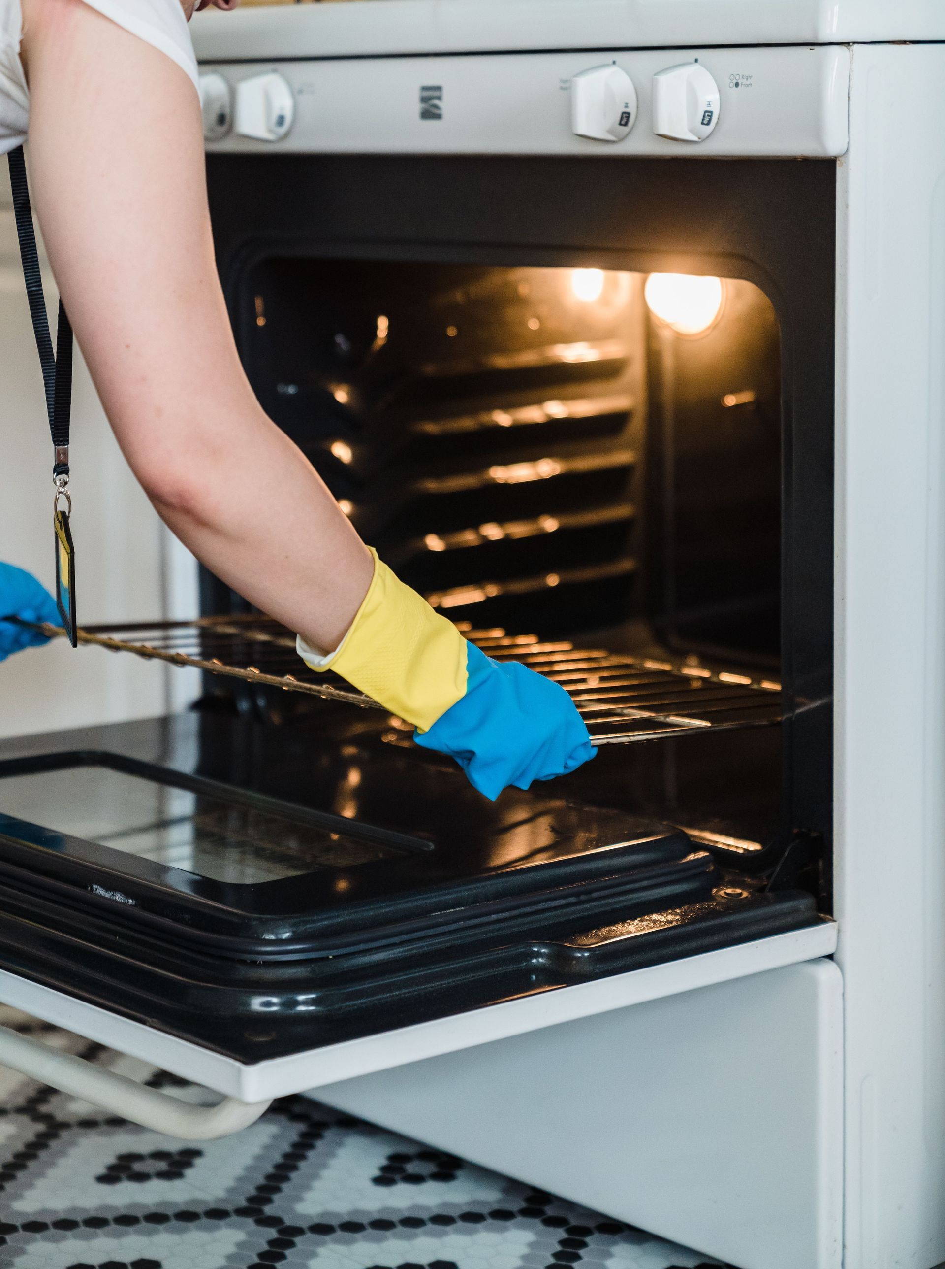 Adult woman cleaning an oven using protective rubber gloves indoors.
